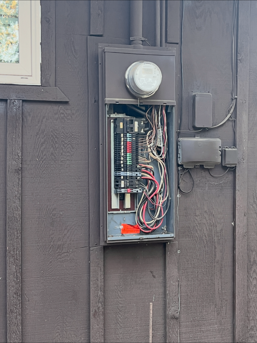 An older electrical panel with its cover removed, showing crowded wiring